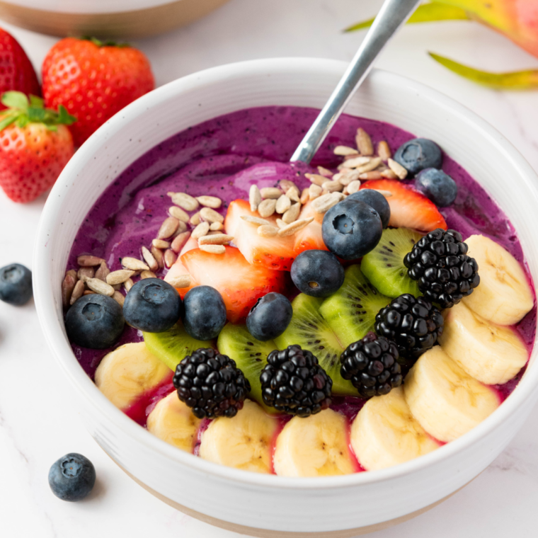 Vibrant dragonfruit yogurt smoothie bowl topped with fresh fruit, granola, and seeds, beautifully presented in a white bowl on a rustic wooden table.