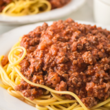 "A steaming plate of Ninja Foodi Spaghetti Bolognese topped with grated Parmesan cheese and fresh basil, served in a rustic bowl."