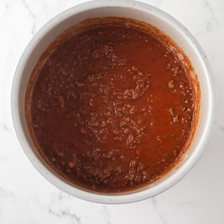 The Bolognese sauce simmering on low heat, thickening and blending flavors over time.