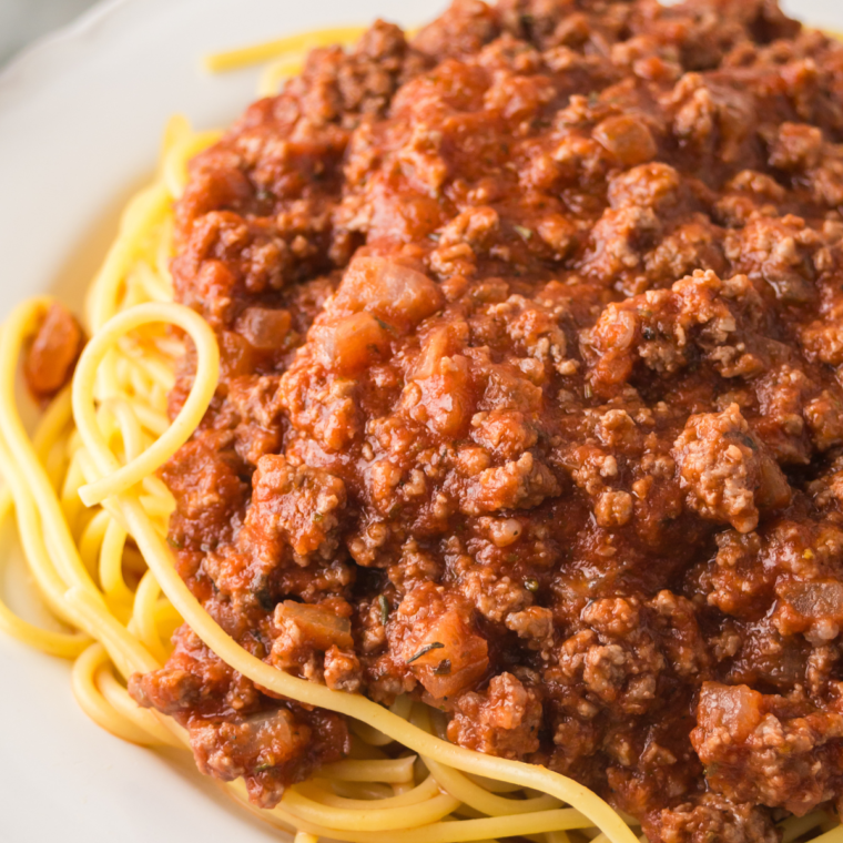 A steaming plate of Ninja Foodi Spaghetti Bolognese topped with grated Parmesan cheese and fresh basil, served in a rustic bowl.