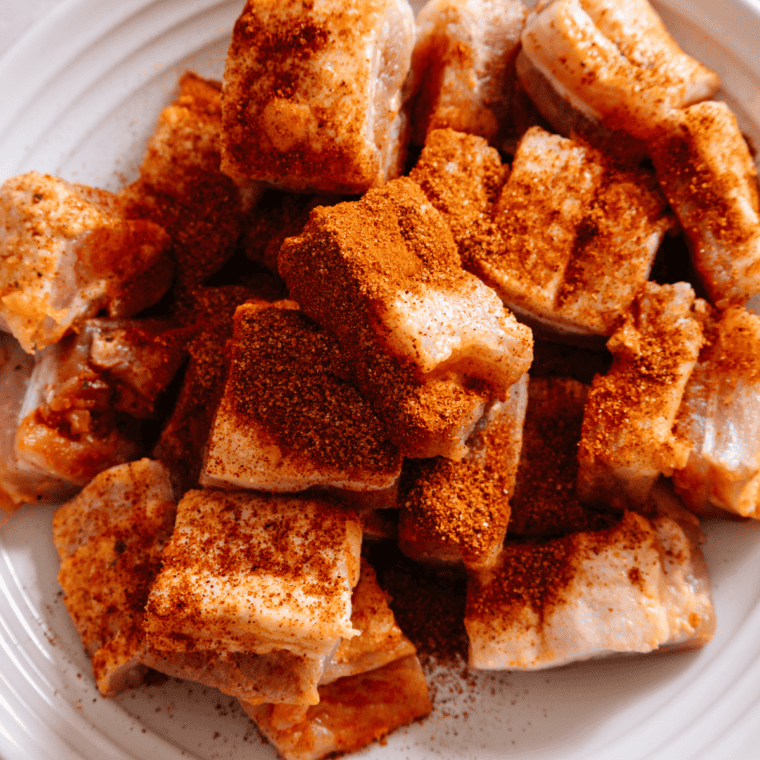 Preparing pork belly bites by coating with steak rub before grilling.