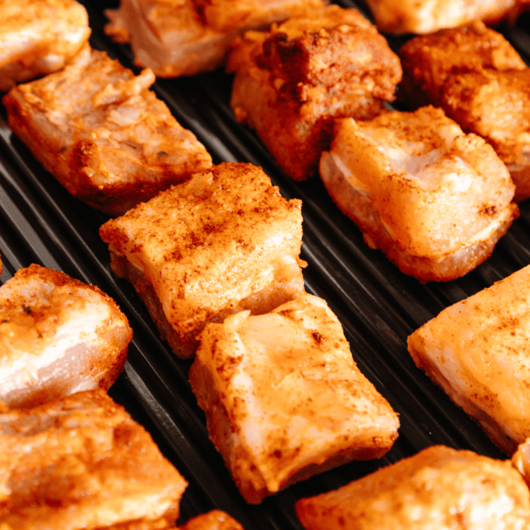 Seared pork belly bites on Ninja Woodfire Grill with lid closed between flips.