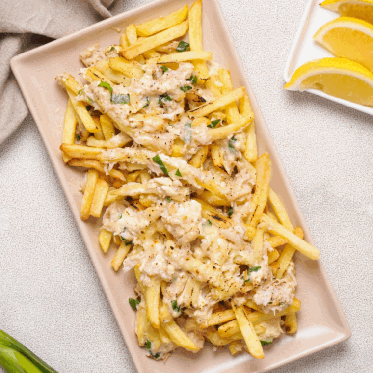 Golden crispy fries loaded with melted cheese, fresh crab meat, and garnished with green onions on a serving plate.