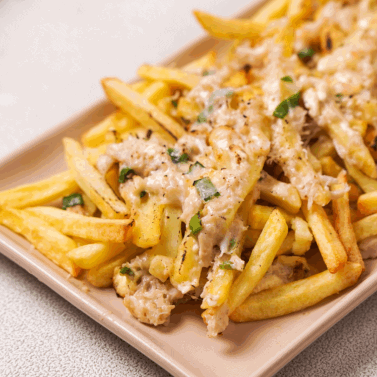 Golden crispy fries topped with creamy crab cheese sauce, melted cheddar, and chopped green onions on a white plate.