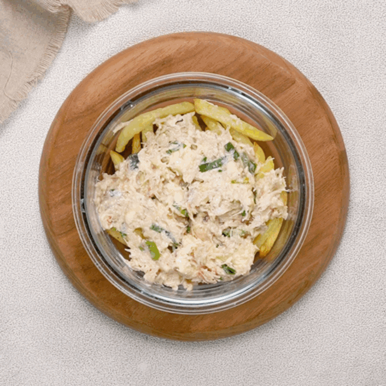 Crab meat evenly spread over golden, crispy fries in preparation for the next step in the recipe.