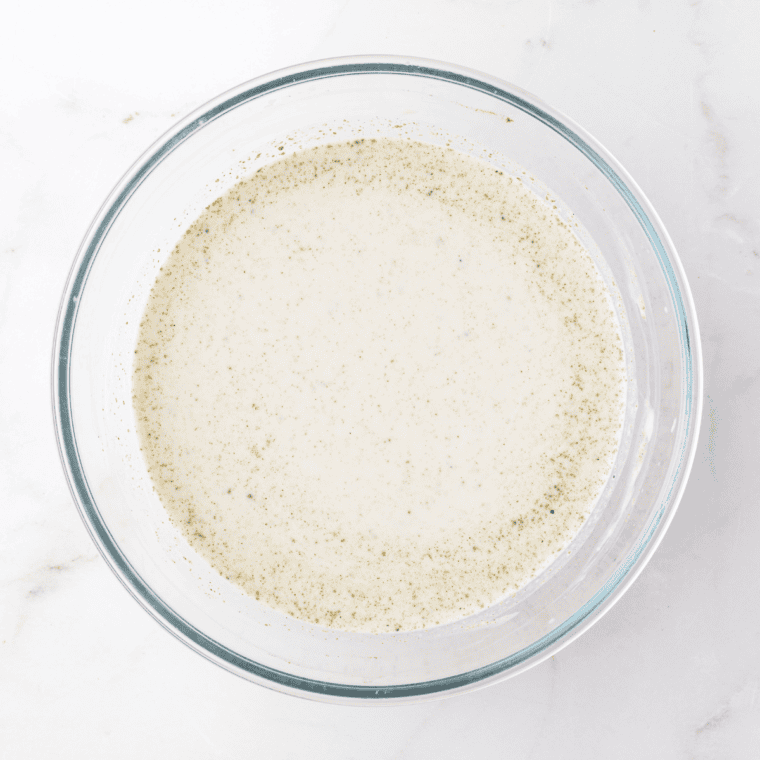 Whisking together cream of mushroom soup, heavy cream, chicken broth, and seasonings in a large bowl.