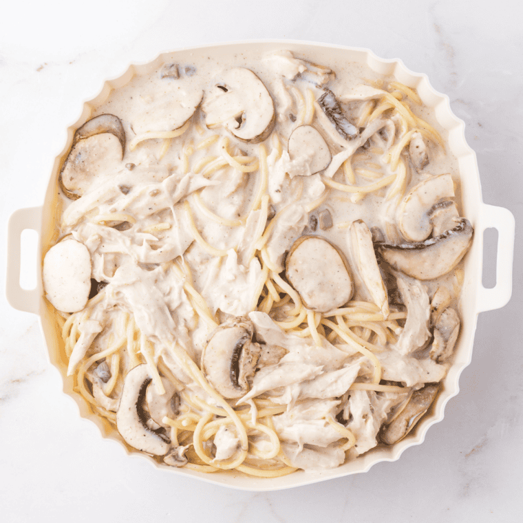 Adding cooked chicken, spaghetti, and mushrooms to the sauce, then transferring to a baking dish, topping with cheese and breadcrumbs.