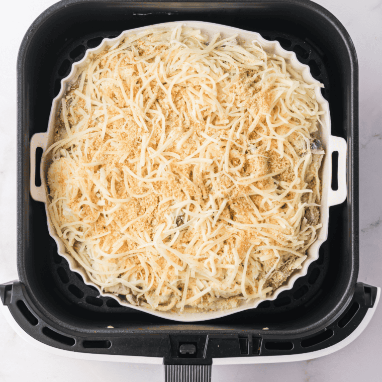 Placing the dish in the air fryer basket to cook, then letting it rest and garnishing with fresh parsley before serving.