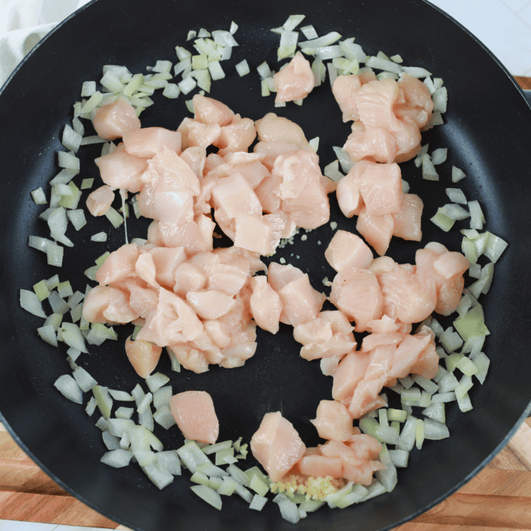 Seasoned diced chicken with salt and black pepper cooking in a skillet with sautéed onions.