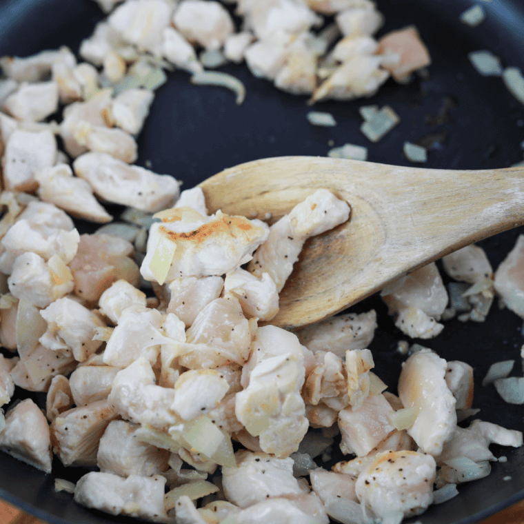 Minced garlic and diced chicken cooking in a skillet until fully cooked.