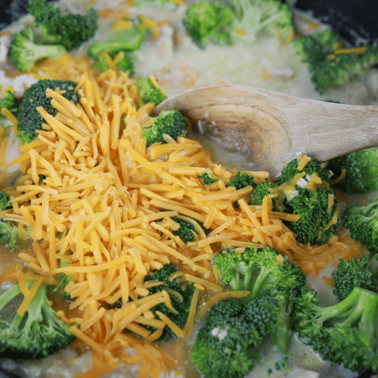 Adding chicken broth, broccoli florets, and shredded cheddar cheese to the skillet, cooking until tender.