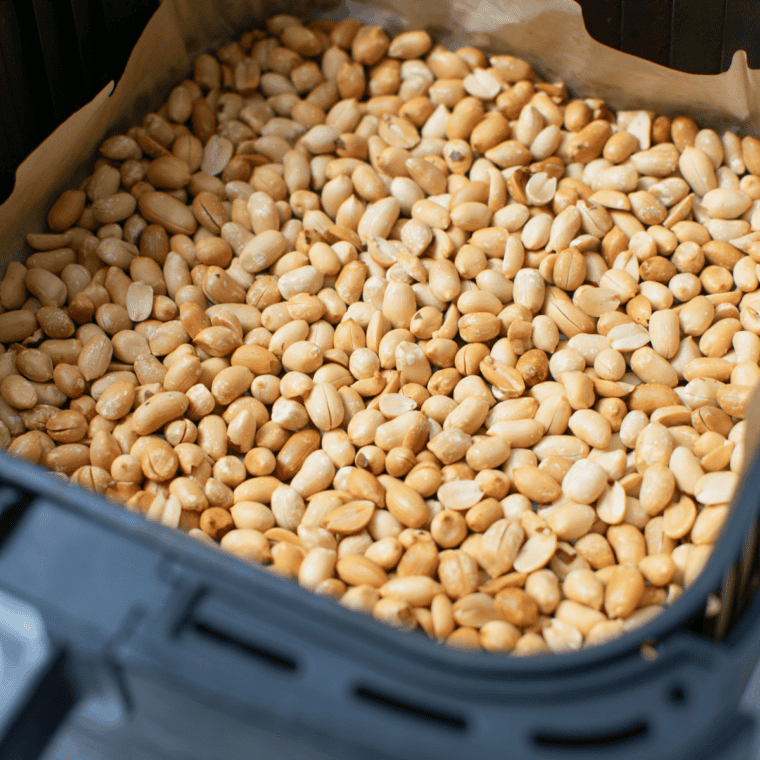 Roasted peanuts in a food processor, blending into a smooth, creamy peanut butter consistency.