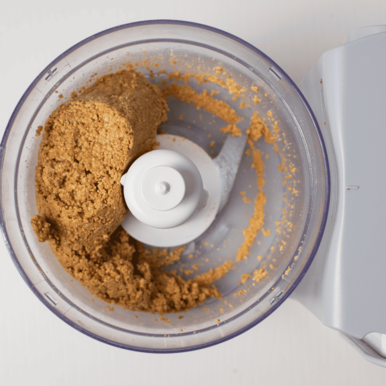 Peanuts blending in a food processor, transforming from powder to a smooth, creamy peanut butter consistency.