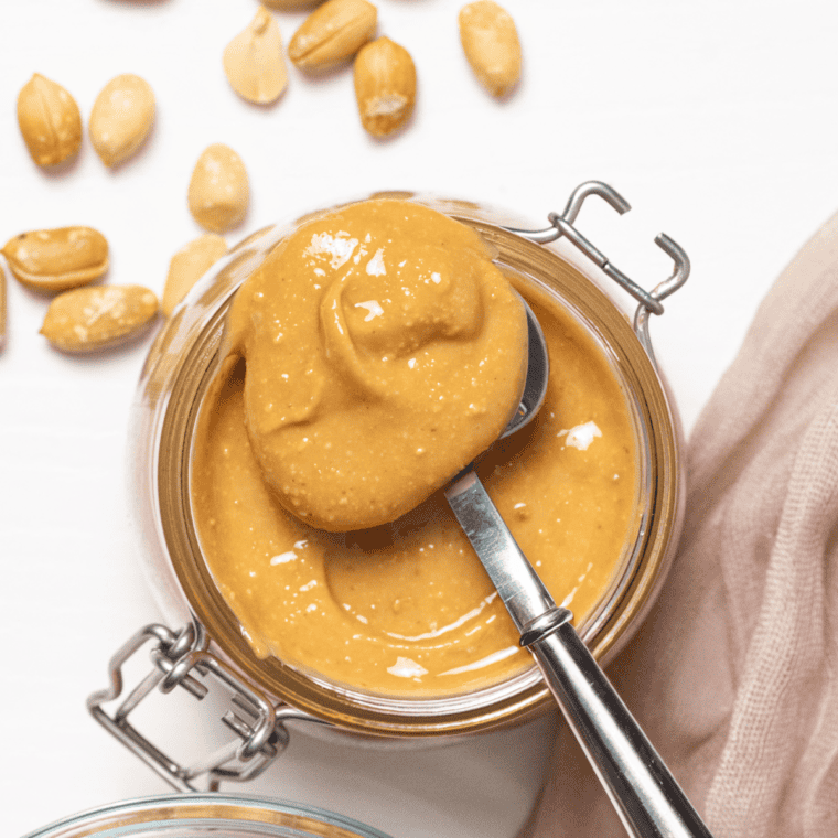 Jar of homemade peanut butter with a spoon, surrounded by roasted peanuts, made using an air fryer.