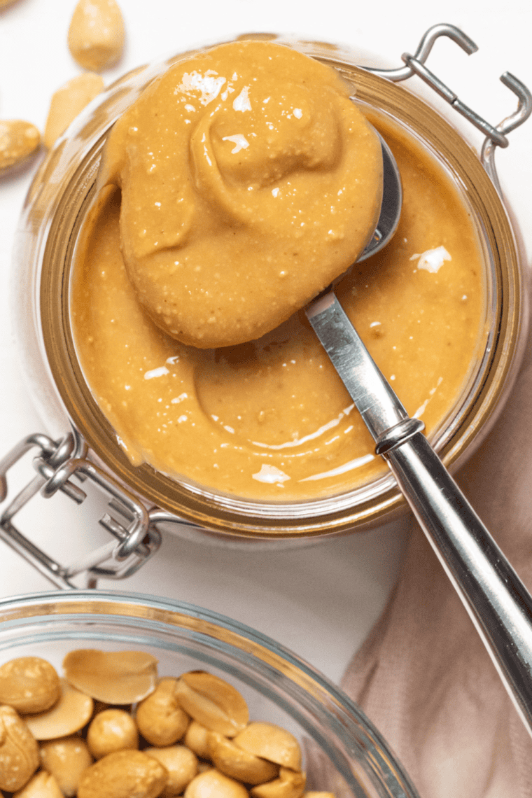 A jar of homemade peanut butter with a spoon, next to freshly roasted peanuts from the air fryer.