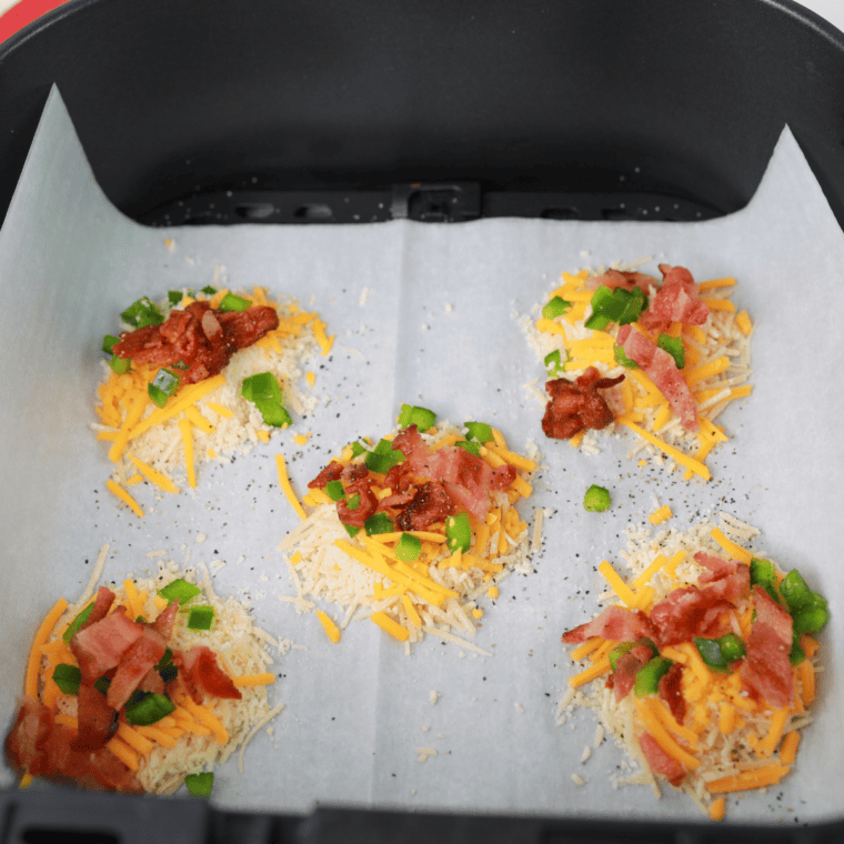 Layer of Parmesan and cheddar cheese topped with diced jalapeño, bacon, and seasoning on parchment paper.