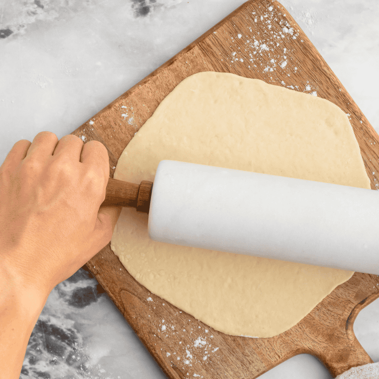 Rolled-out pizza dough in an air fryer basket, brushed with olive oil for a crispy crust.