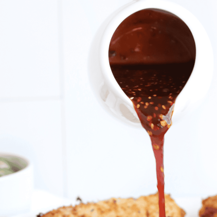 Ancho Chile BBQ Sauce in a jar with a spoon, showing its rich, smoky texture and vibrant color.