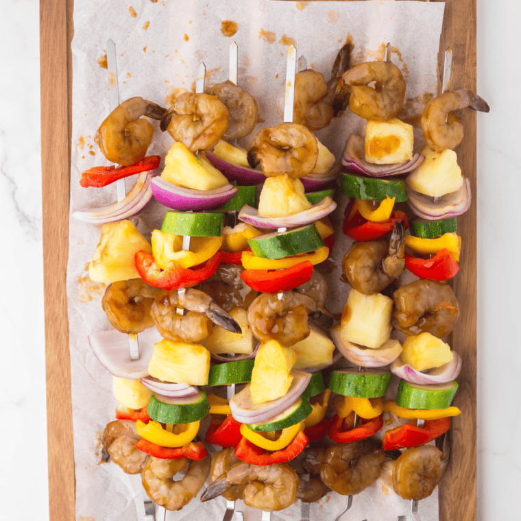 Shrimp, bell peppers, onions, zucchini, and pineapple arranged on skewers.