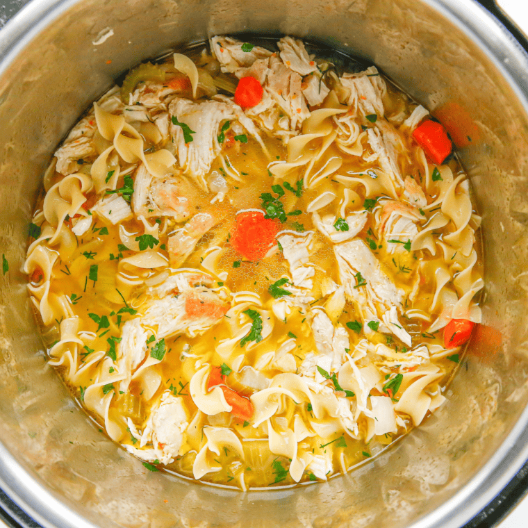 Adding egg noodles and shredded chicken to the soup, simmering until tender and flavorful.