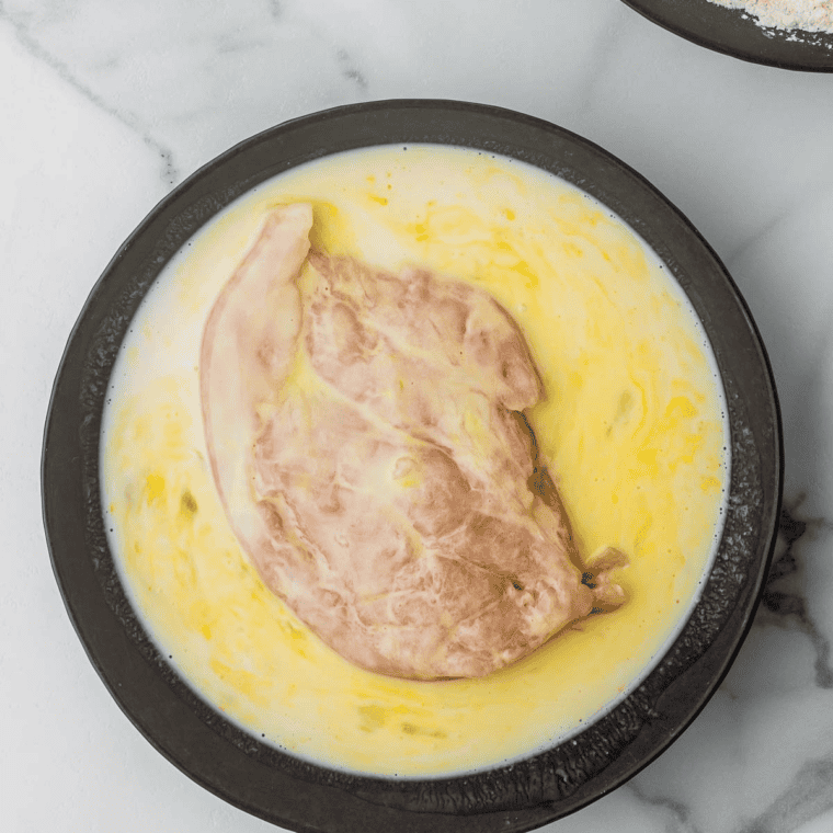 Coating chicken breasts in beaten egg and seasoned flour mixture for air fryer.