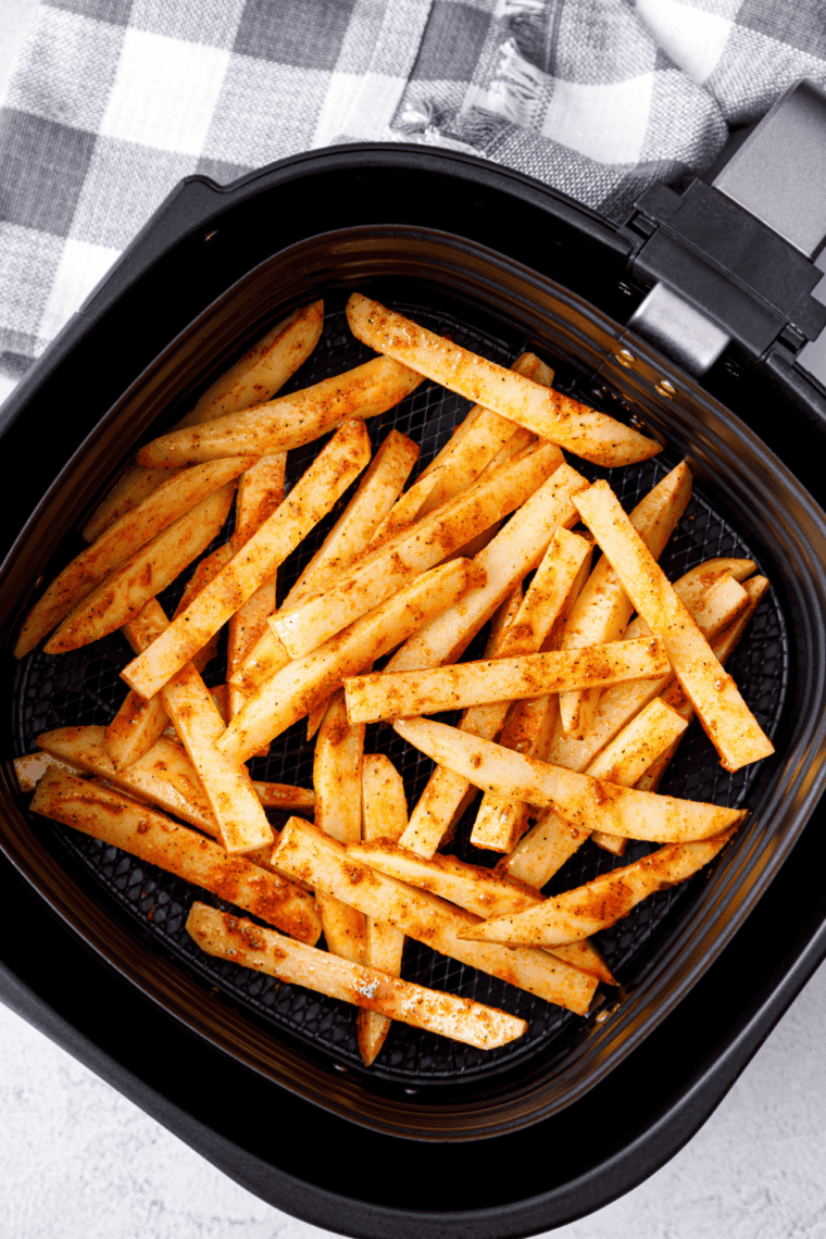 Seasoned fries cooking in an air fryer basket until crispy and golden brown.