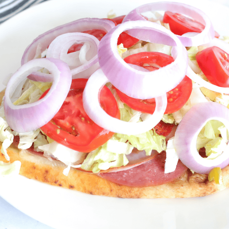 Add shredded iceberg lettuce, tomatoes, onions, dill pickles, and mustard, then top with the hoagie roll to complete the sandwich.