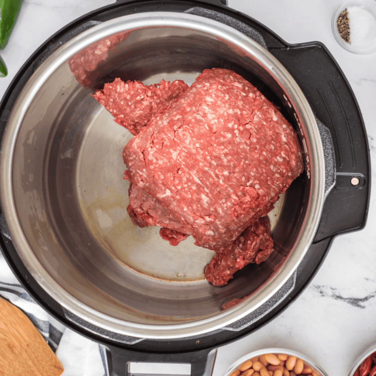 Ground beef cooking in a Dutch oven with oil over medium heat, being broken apart as it browns.