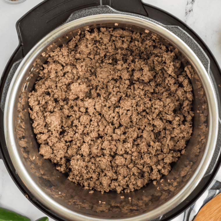 Seasonings being stirred into browned ground beef in a Dutch oven to enhance the flavors.