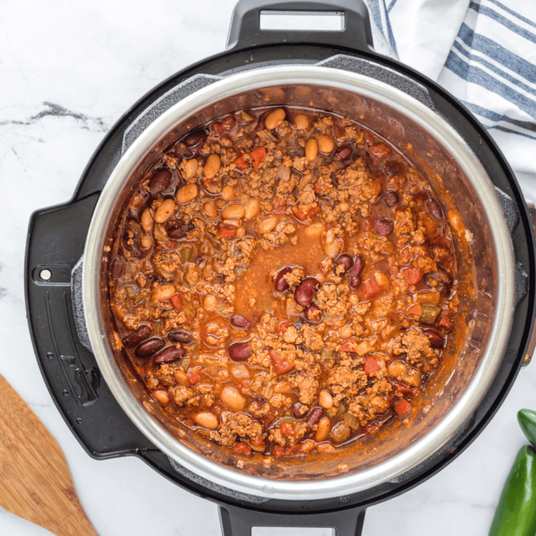 French onion soup, tomato sauce, cola, and liquid smoke being poured into a pot of chili with kidney beans, simmering to perfection.