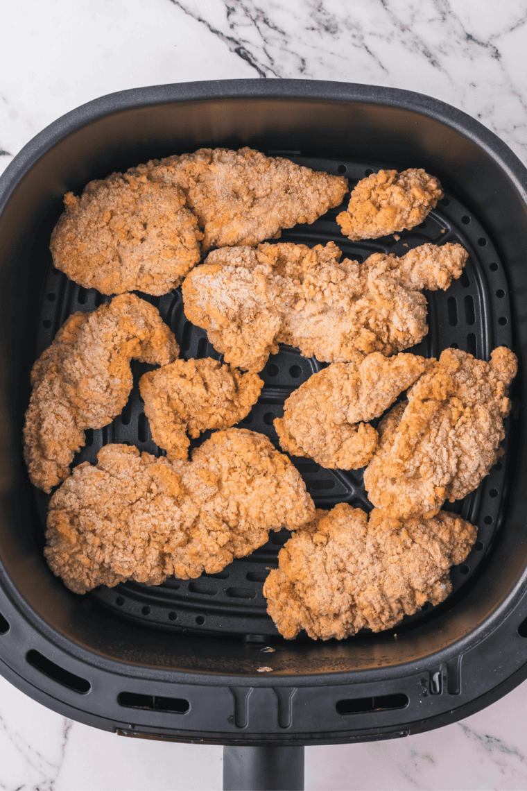 Preheating air fryer, cooking frozen chicken tenders until crispy, and slicing into bite-sized pieces.