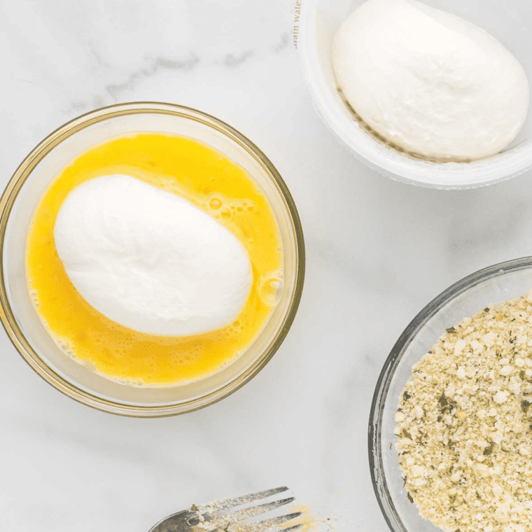 Coating the burrata ball in beaten egg for breading.