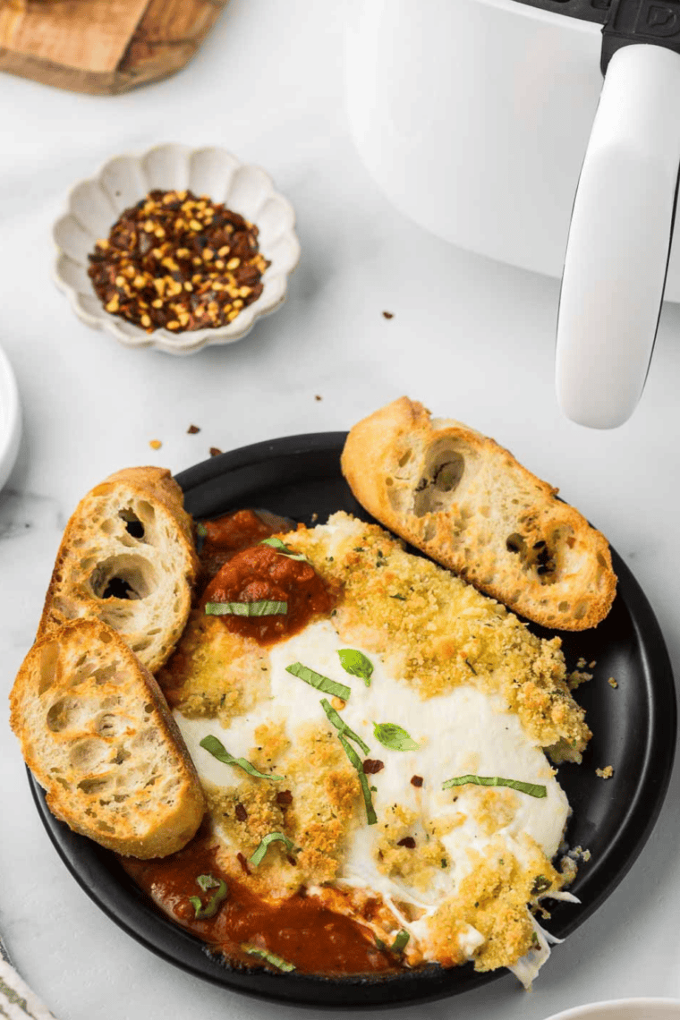 Air Fryer Burrata with golden crispy crust and creamy center, garnished with fresh basil and served with marinara sauce.