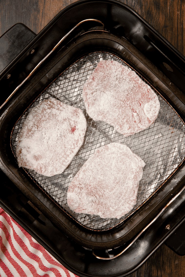 Coated steak pieces placed in the air fryer basket, drizzled with olive oil, and air fried until golden brown.