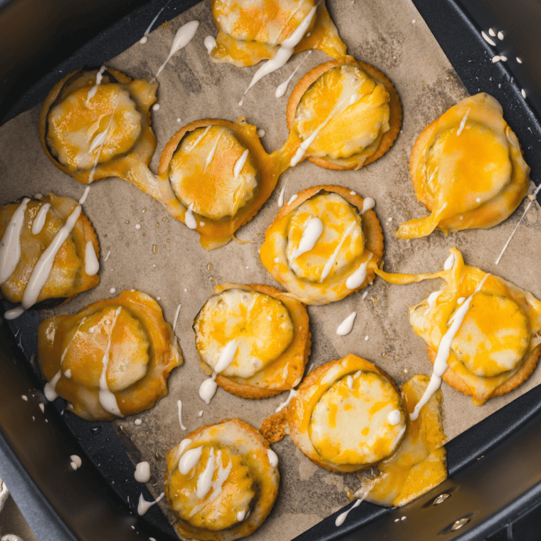 Air Fryer Basket with golden-brown Cheesy Ritz Pickle Bites with melted cheese and pickles sandwiched between crispy crackers.. 