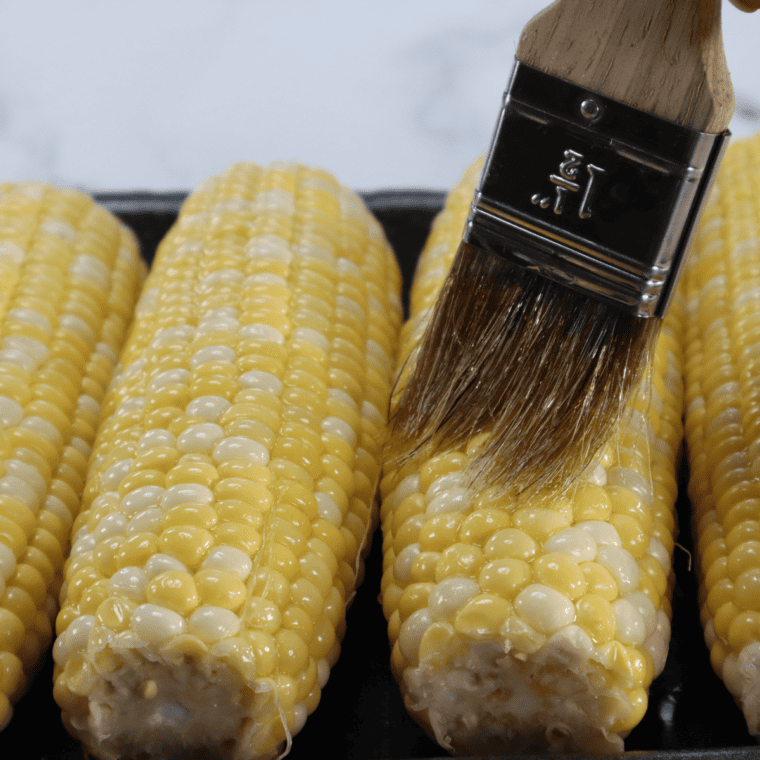 Removing husks from corn, cutting ears to fit air fryer, and brushing with olive oil to prevent sticking