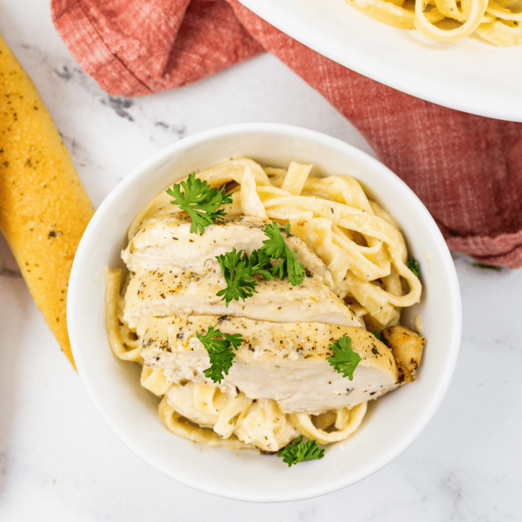 A bowl of creamy Copycat Carrabba’s Alfredo sauce served over fettuccine, garnished with Parmesan cheese and fresh parsley.