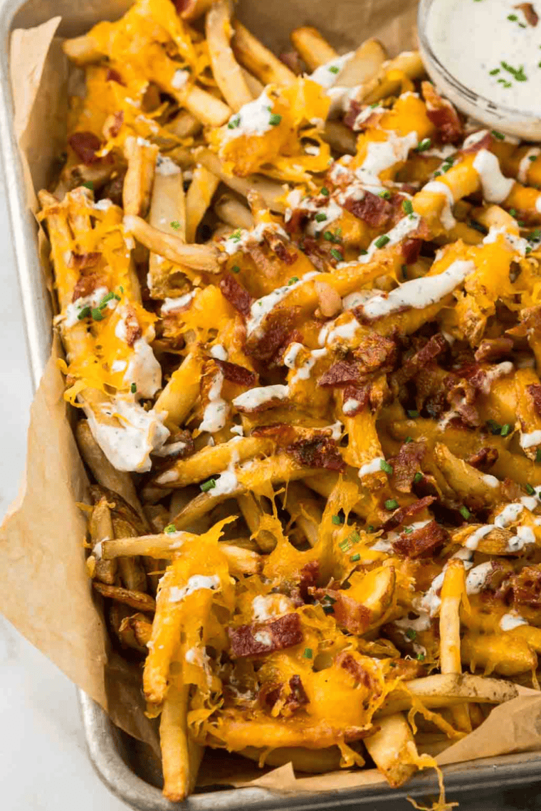 A plate of crispy Texas Cheese Fries topped with melted cheese, crispy bacon, and sliced jalapeños, served with a side of ranch dressing.