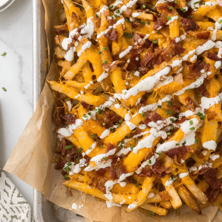 A plate of Copycat Chili’s Texas Cheese Fries topped with melted cheese, crispy bacon, and sliced jalapeños, served with a side of ranch dressing.