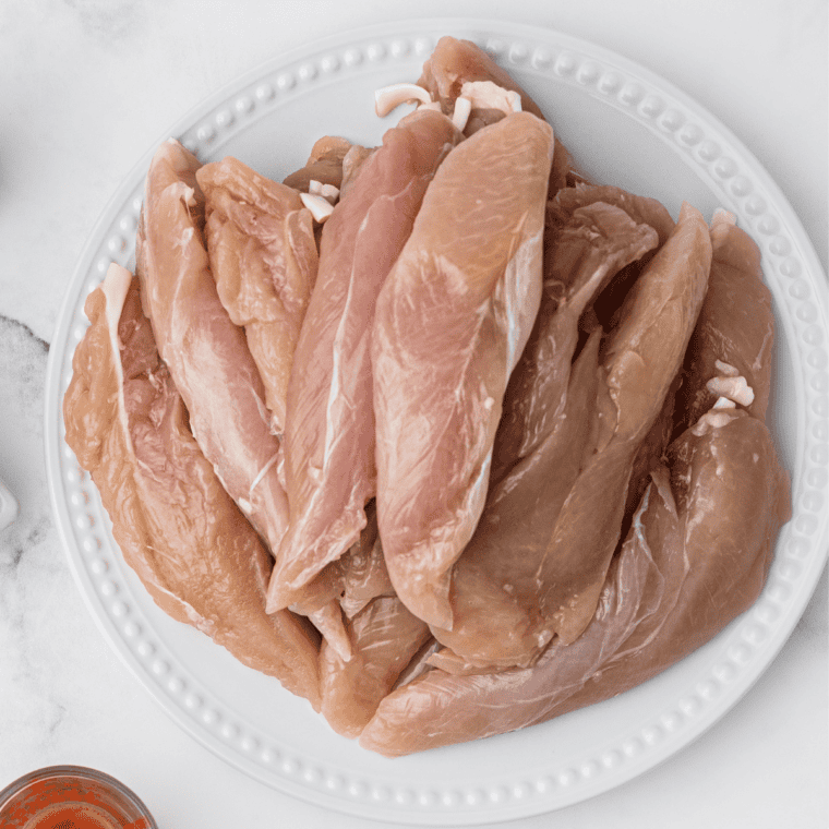 Sliced raw chicken breast fillets on a plate.