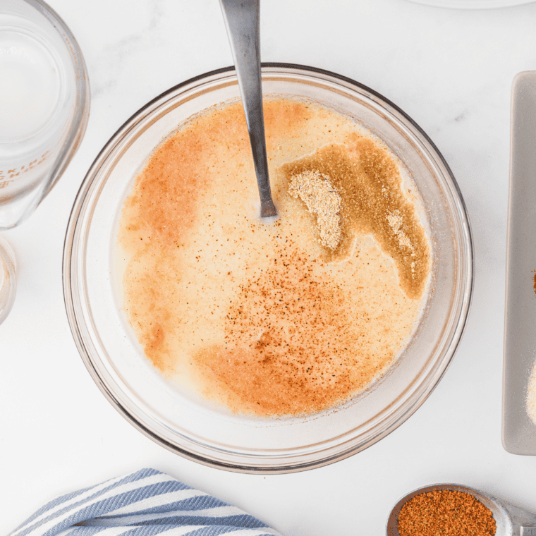 A large mixing bowl containing all-purpose flour blended with dried herbs and spices, including thyme, basil, oregano, garlic salt, dried mustard, onion powder, ginger powder, black pepper, white pepper, paprika, cayenne pepper, and celery salt, evenly combined.