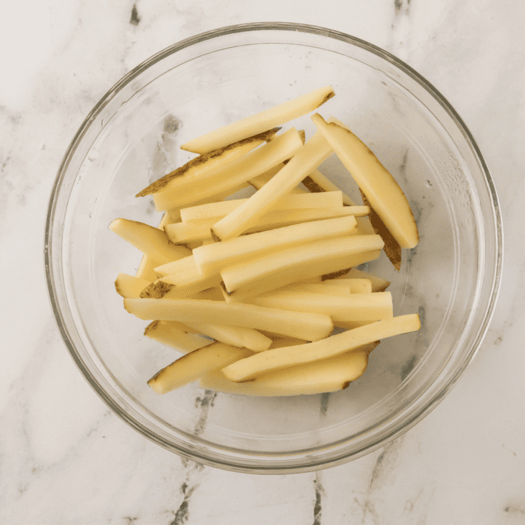 Prepare the Potatoes – Fresh russet potatoes cut into fries, ready for soaking.