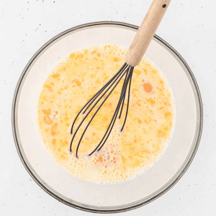 Beating eggs in a clear bowl with a whisk.