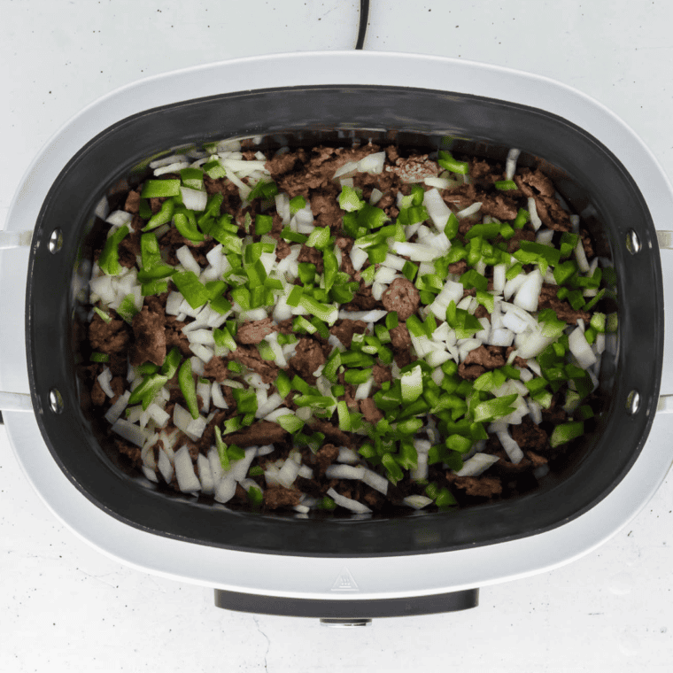 Layering hash browns, cooked sausage, peppers, and onions in the cooker for a delicious breakfast casserole.