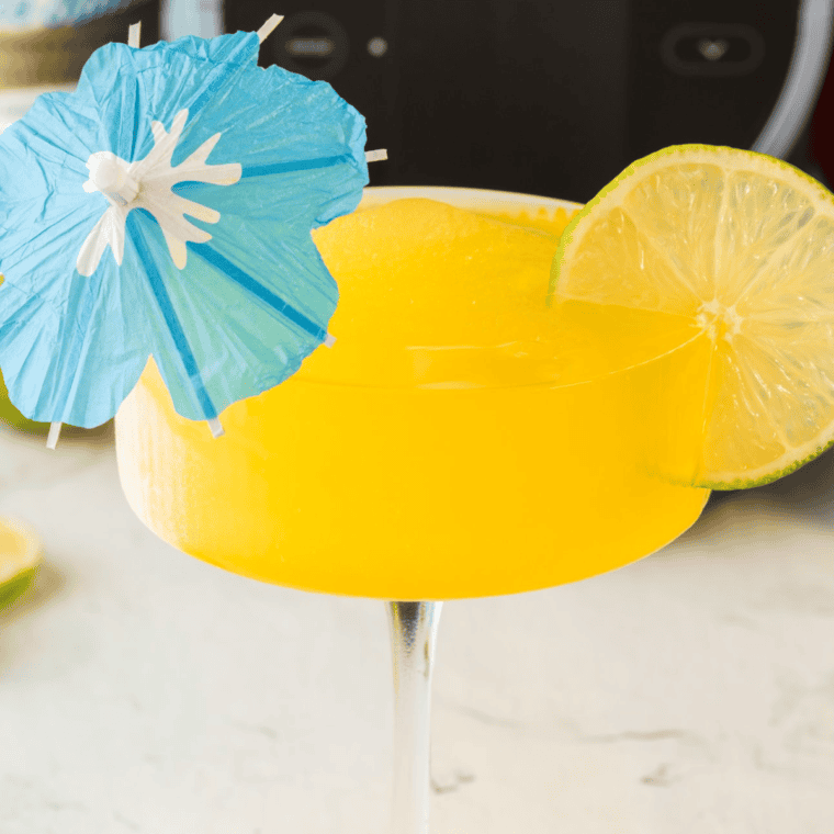  "A frosty Ninja Slushi Mango Daiquiri served in a glass with a lime garnish and tropical fruit."







