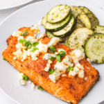 Crispy Air Fryer Buffalo Salmon fillet topped with buffalo sauce and garnished with herbs on a plate.
