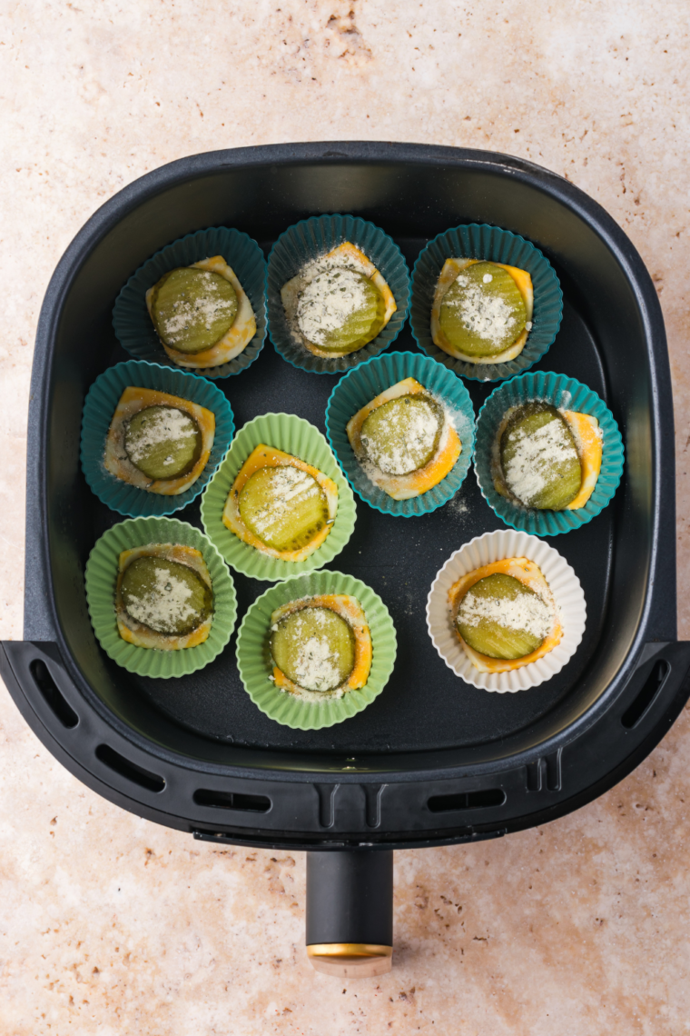 Pickle chip placed on cheese in muffin tin, sprinkled with ranch seasoning and topped with more shredded cheese.