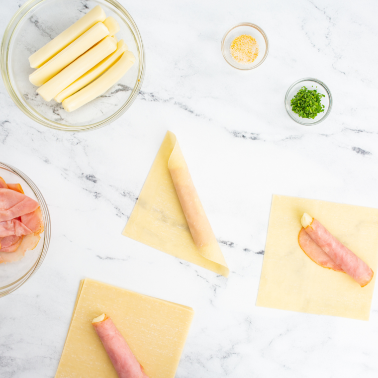 Brushing egg wash on the edges of a wonton wrapper and folding it around ham and mozzarella to create a sealed pocket.