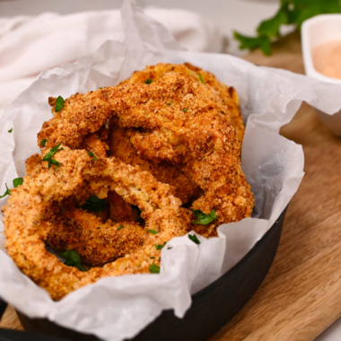 Golden, crispy keto onion rings cooked in the air fryer and served with a dipping sauce on a white plate.