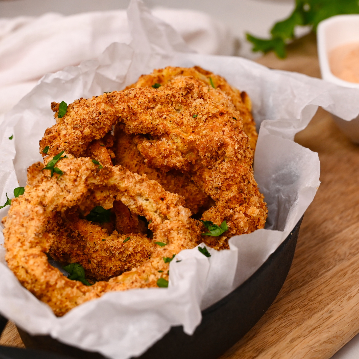 Golden, crispy keto onion rings cooked in the air fryer and served with a dipping sauce on a white plate.